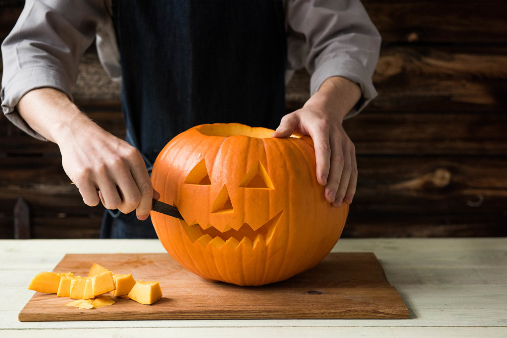 Saisonal essen Halloween: Mann schnitzt Gesicht in einen Kürbis